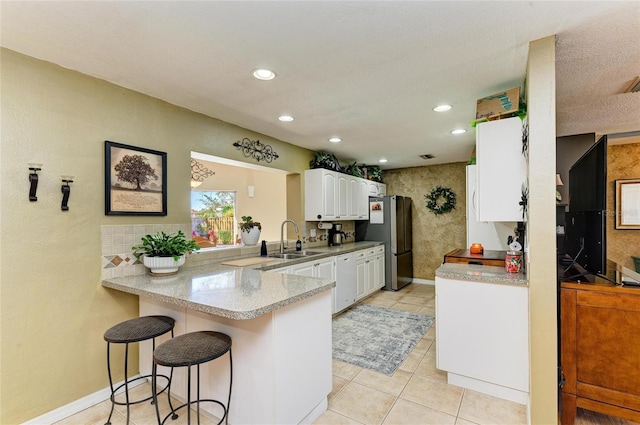 kitchen featuring a sink, a kitchen breakfast bar, white cabinetry, freestanding refrigerator, and a peninsula