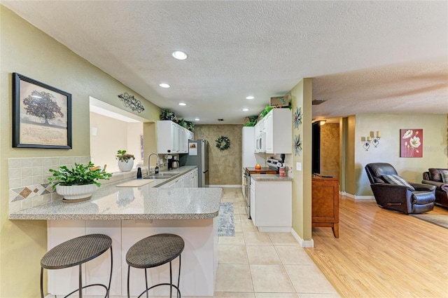 kitchen featuring a kitchen bar, appliances with stainless steel finishes, a peninsula, white cabinetry, and a sink