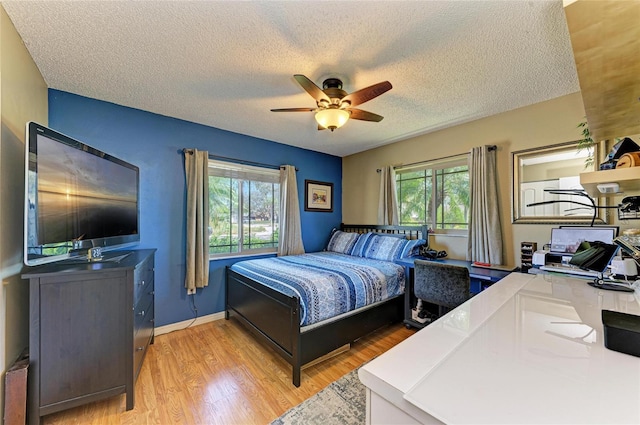 bedroom with ceiling fan, multiple windows, light wood-type flooring, and a textured ceiling