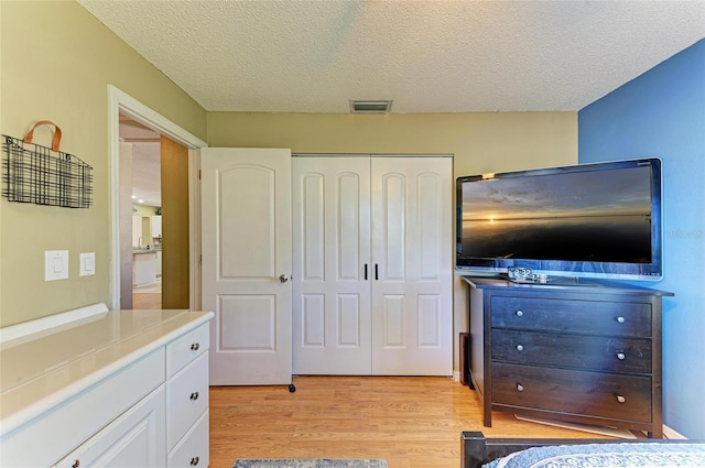 bedroom featuring visible vents, light wood-style floors, a closet, and a textured ceiling