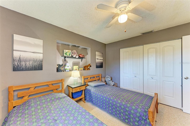 carpeted bedroom with a closet, visible vents, a textured ceiling, and a ceiling fan