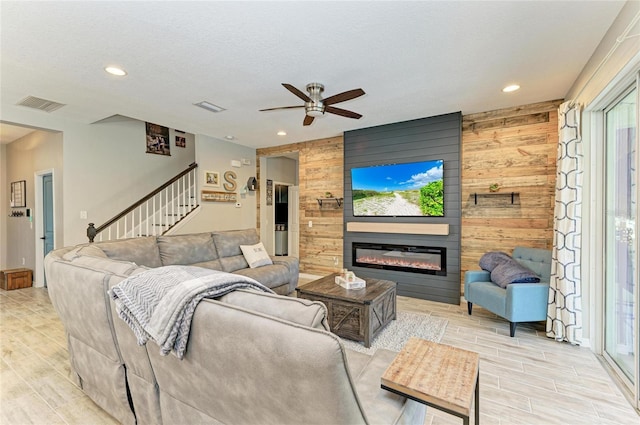 living area featuring wooden walls, visible vents, a glass covered fireplace, and wood finish floors