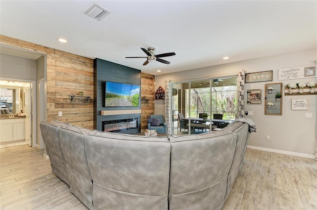 living area featuring a fireplace, light wood finished floors, visible vents, a ceiling fan, and wooden walls