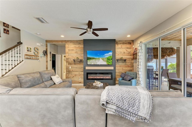 carpeted living area featuring a glass covered fireplace, visible vents, wooden walls, and a textured ceiling