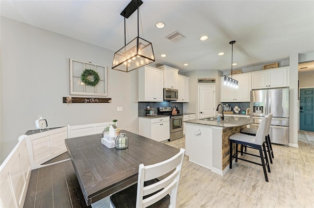 kitchen featuring stainless steel appliances, visible vents, backsplash, a sink, and a kitchen breakfast bar