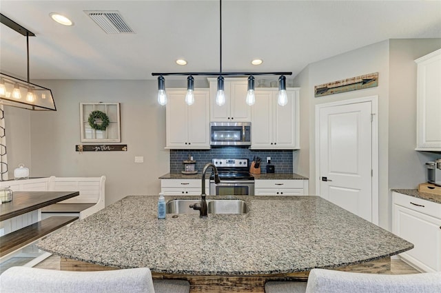 kitchen featuring tasteful backsplash, a center island with sink, visible vents, appliances with stainless steel finishes, and a sink