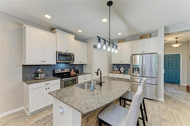 kitchen featuring a kitchen breakfast bar, a kitchen island with sink, stainless steel appliances, white cabinetry, and a sink