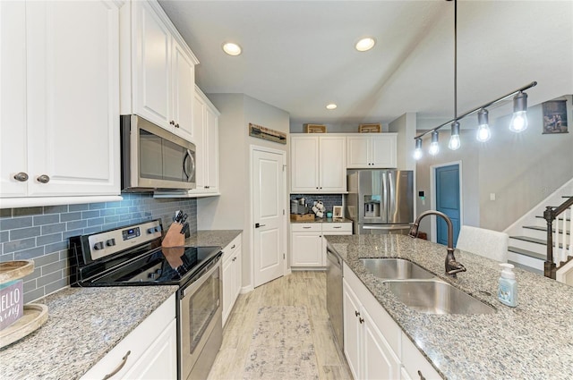 kitchen featuring stainless steel appliances, tasteful backsplash, white cabinetry, a sink, and light wood-type flooring