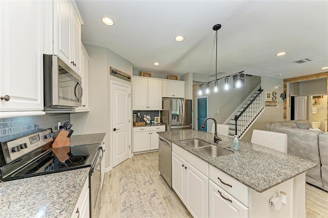 kitchen with stainless steel appliances, visible vents, light wood-style floors, and an island with sink