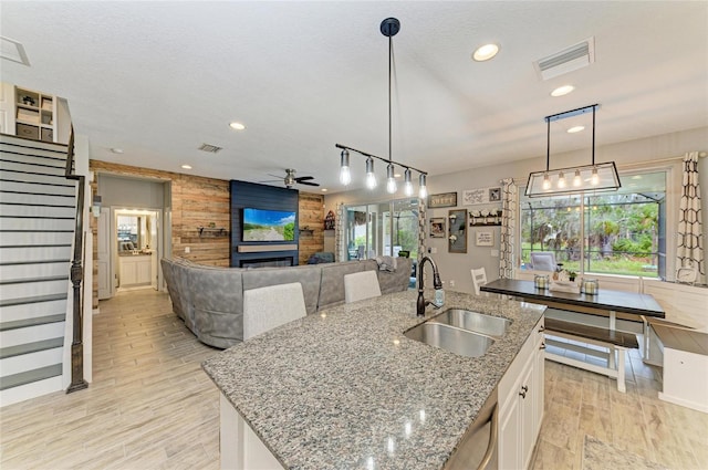 kitchen with wooden walls, visible vents, white cabinets, a fireplace, and a sink