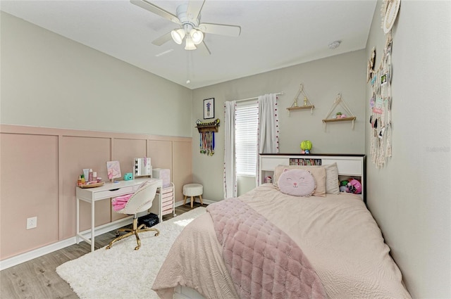 bedroom with a wainscoted wall, ceiling fan, a decorative wall, and wood finished floors