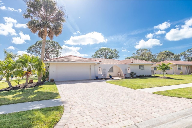 mediterranean / spanish house with an attached garage, a tile roof, decorative driveway, stucco siding, and a front lawn