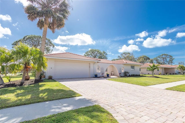 mediterranean / spanish-style home featuring a garage, a tile roof, decorative driveway, stucco siding, and a front yard