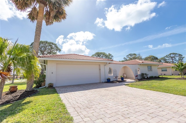 mediterranean / spanish home featuring a garage, a tiled roof, decorative driveway, stucco siding, and a front yard