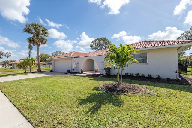 mediterranean / spanish home with stucco siding, an attached garage, driveway, a tiled roof, and a front lawn