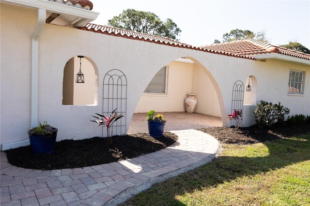 view of side of property with a patio, a tile roof, and stucco siding