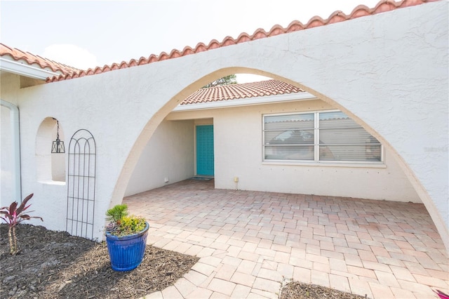 entrance to property with a patio area, a tiled roof, and stucco siding