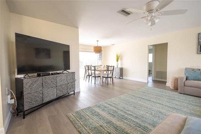 living room with ceiling fan, wood finished floors, visible vents, and baseboards