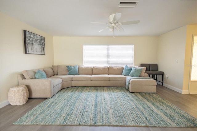 living area featuring a ceiling fan, visible vents, baseboards, and wood finished floors