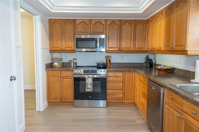 kitchen with stainless steel appliances, light wood finished floors, brown cabinetry, and baseboards