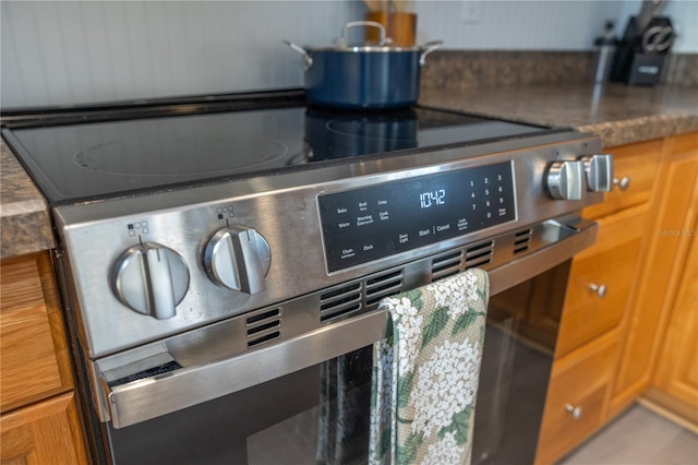 interior details featuring dark countertops, stainless steel range with electric stovetop, and brown cabinets