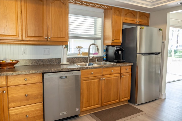 kitchen with light wood finished floors, dark countertops, brown cabinets, stainless steel appliances, and a sink