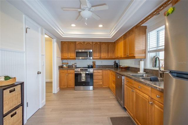 kitchen with a tray ceiling, appliances with stainless steel finishes, a sink, and brown cabinets