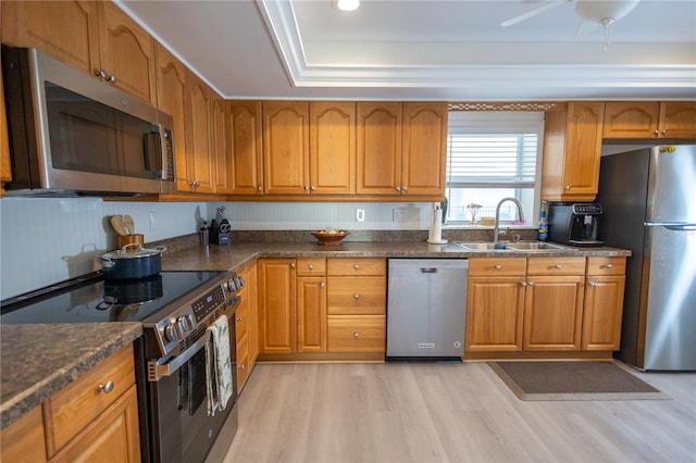 kitchen with brown cabinetry, light wood-style floors, stainless steel appliances, and a sink