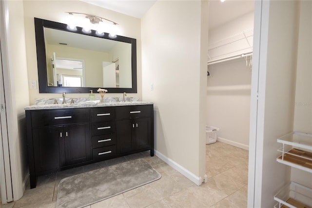 bathroom featuring a sink, a spacious closet, baseboards, and double vanity