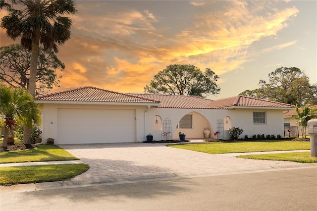 mediterranean / spanish home with an attached garage, a tiled roof, and a front lawn