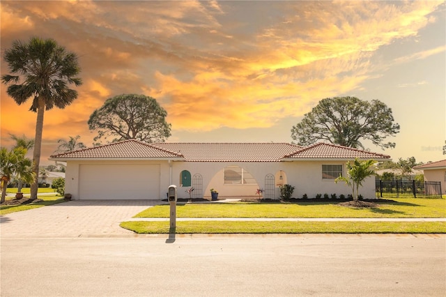 mediterranean / spanish home featuring a tile roof, an attached garage, fence, decorative driveway, and a yard