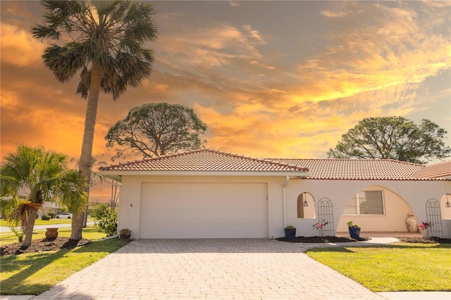 mediterranean / spanish house with a garage, a tiled roof, decorative driveway, and stucco siding