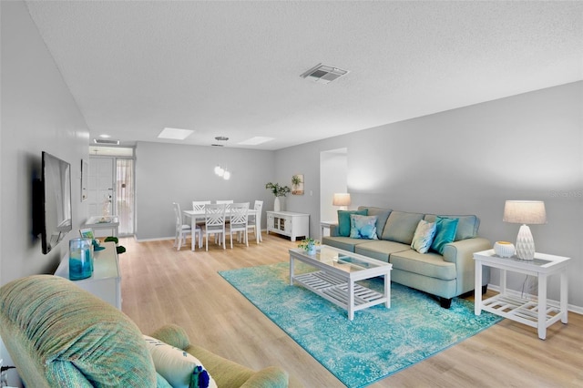 living area featuring baseboards, visible vents, a textured ceiling, and light wood finished floors