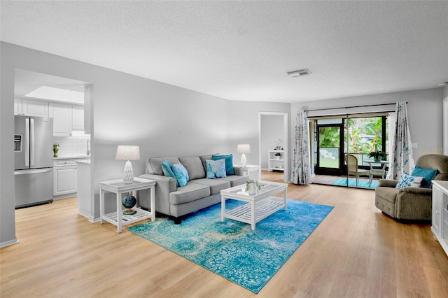 living area with light wood-type flooring, visible vents, and a textured ceiling