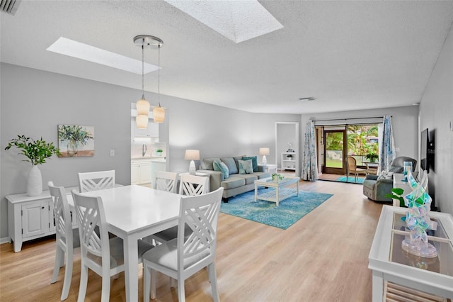 dining room with light wood-type flooring, a skylight, visible vents, and a textured ceiling