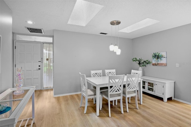 dining space with light wood-type flooring, a skylight, visible vents, and a textured ceiling