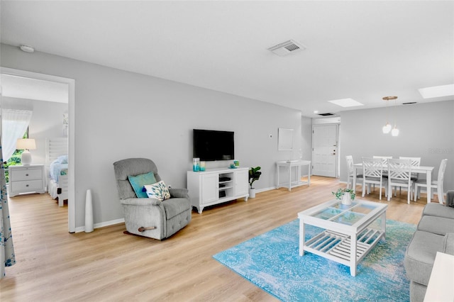 living room with a skylight, visible vents, light wood-style flooring, and baseboards