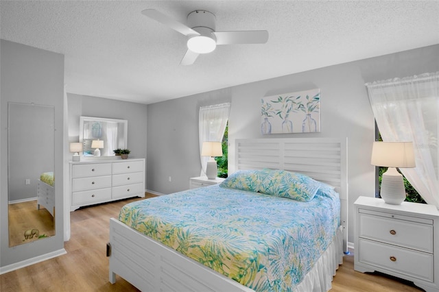 bedroom with a textured ceiling, baseboards, light wood-style flooring, and a ceiling fan