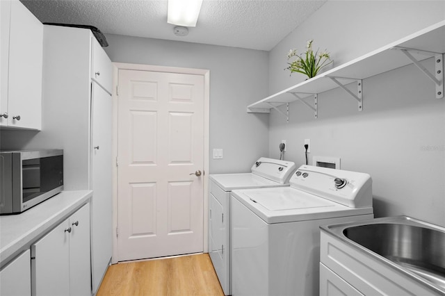 laundry room with a textured ceiling, a sink, light wood-type flooring, independent washer and dryer, and cabinet space