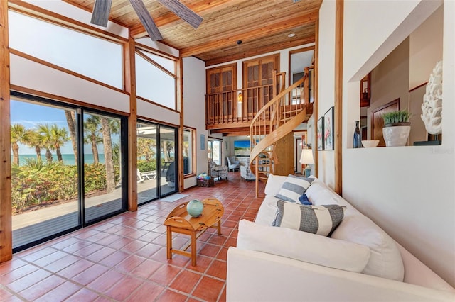 tiled living room featuring beam ceiling, a towering ceiling, a ceiling fan, wooden ceiling, and stairs