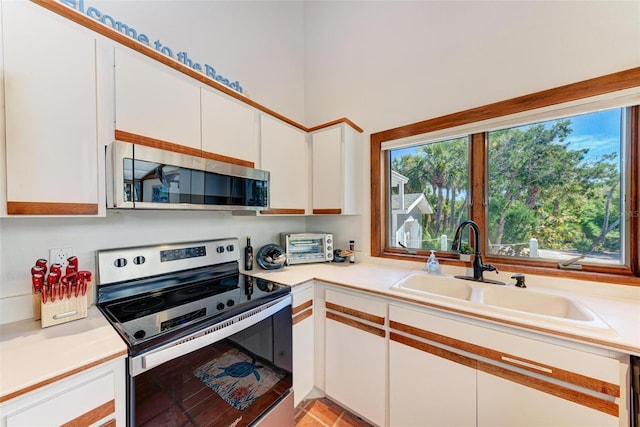 kitchen with a toaster, stainless steel appliances, a sink, white cabinetry, and light countertops