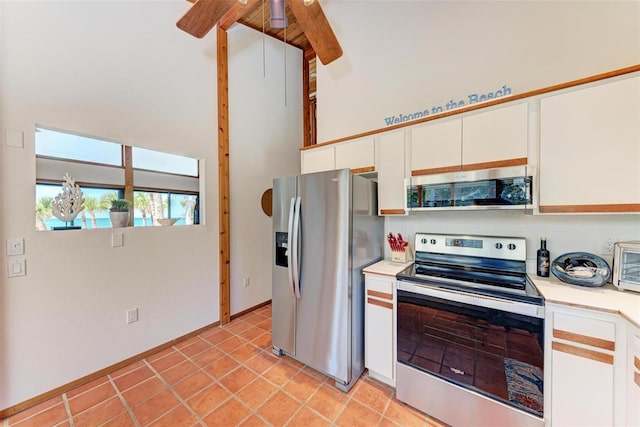 kitchen featuring beam ceiling, light countertops, a high ceiling, appliances with stainless steel finishes, and white cabinetry