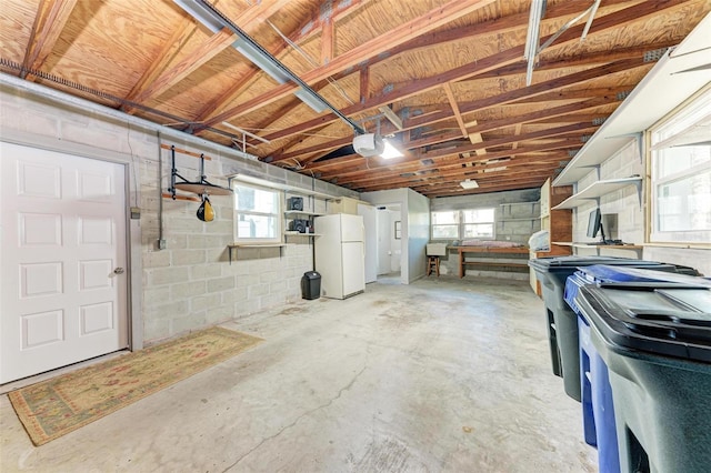 garage with a garage door opener, freestanding refrigerator, and concrete block wall