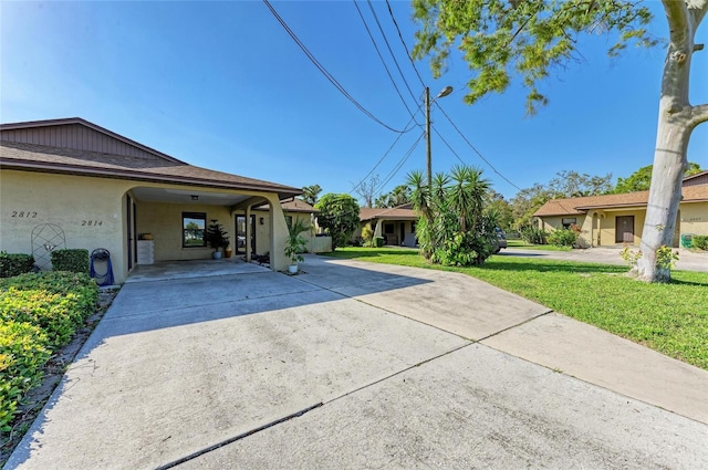 view of home's exterior with an attached carport, concrete driveway, a lawn, roof with shingles, and stucco siding