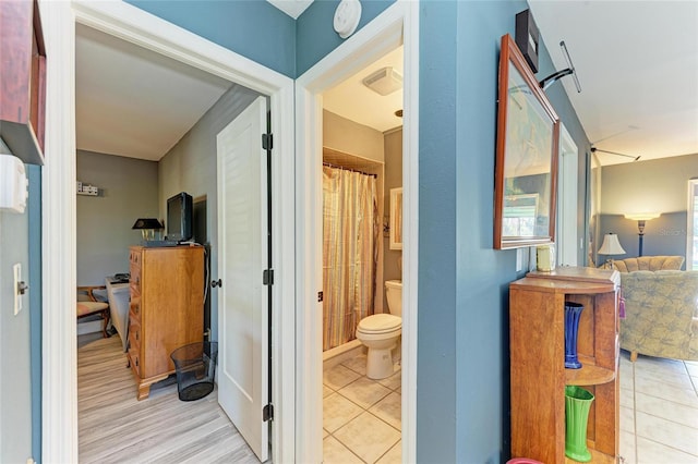 interior space with tile patterned flooring, a shower with curtain, connected bathroom, and toilet