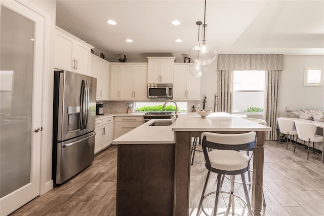 kitchen featuring stainless steel appliances, tasteful backsplash, light countertops, a sink, and wood finished floors