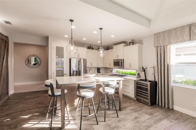 kitchen featuring light countertops, visible vents, appliances with stainless steel finishes, beverage cooler, and a kitchen breakfast bar