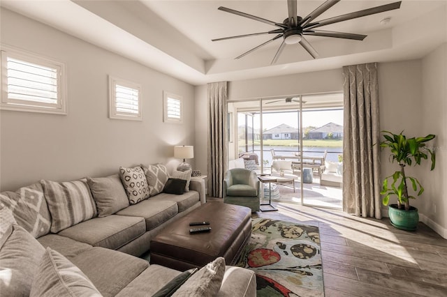 living area with wood finished floors, a raised ceiling, a ceiling fan, and baseboards