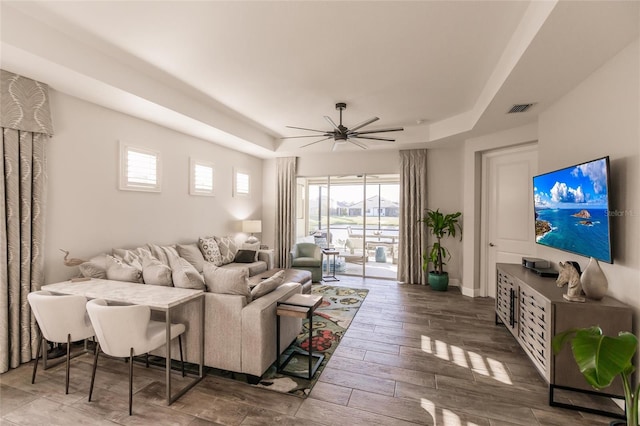 living area featuring a tray ceiling, visible vents, a ceiling fan, wood finished floors, and baseboards