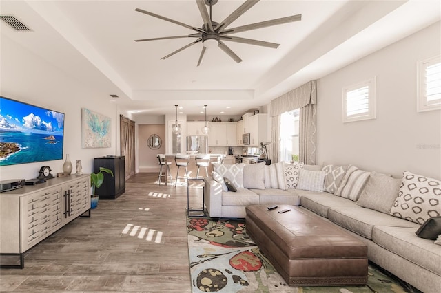 living area featuring visible vents, baseboards, a ceiling fan, wood finished floors, and a tray ceiling